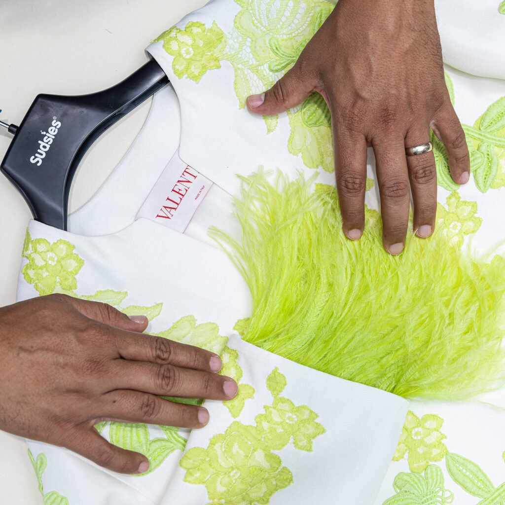 Hands inspecting a Valentino garment with neon feather detailing on a Sudsies hanger.