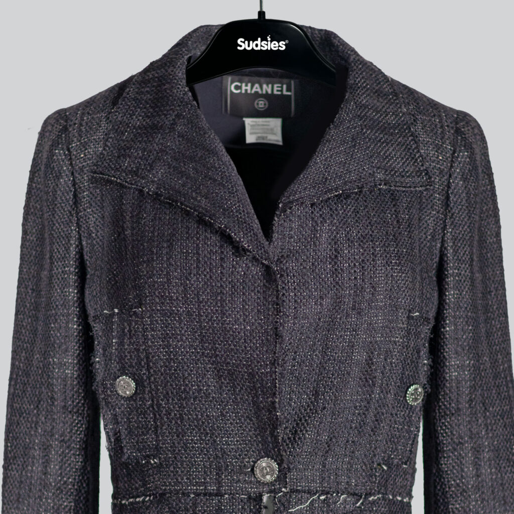 Chanel jacket displayed on a black Sudsies hanger.